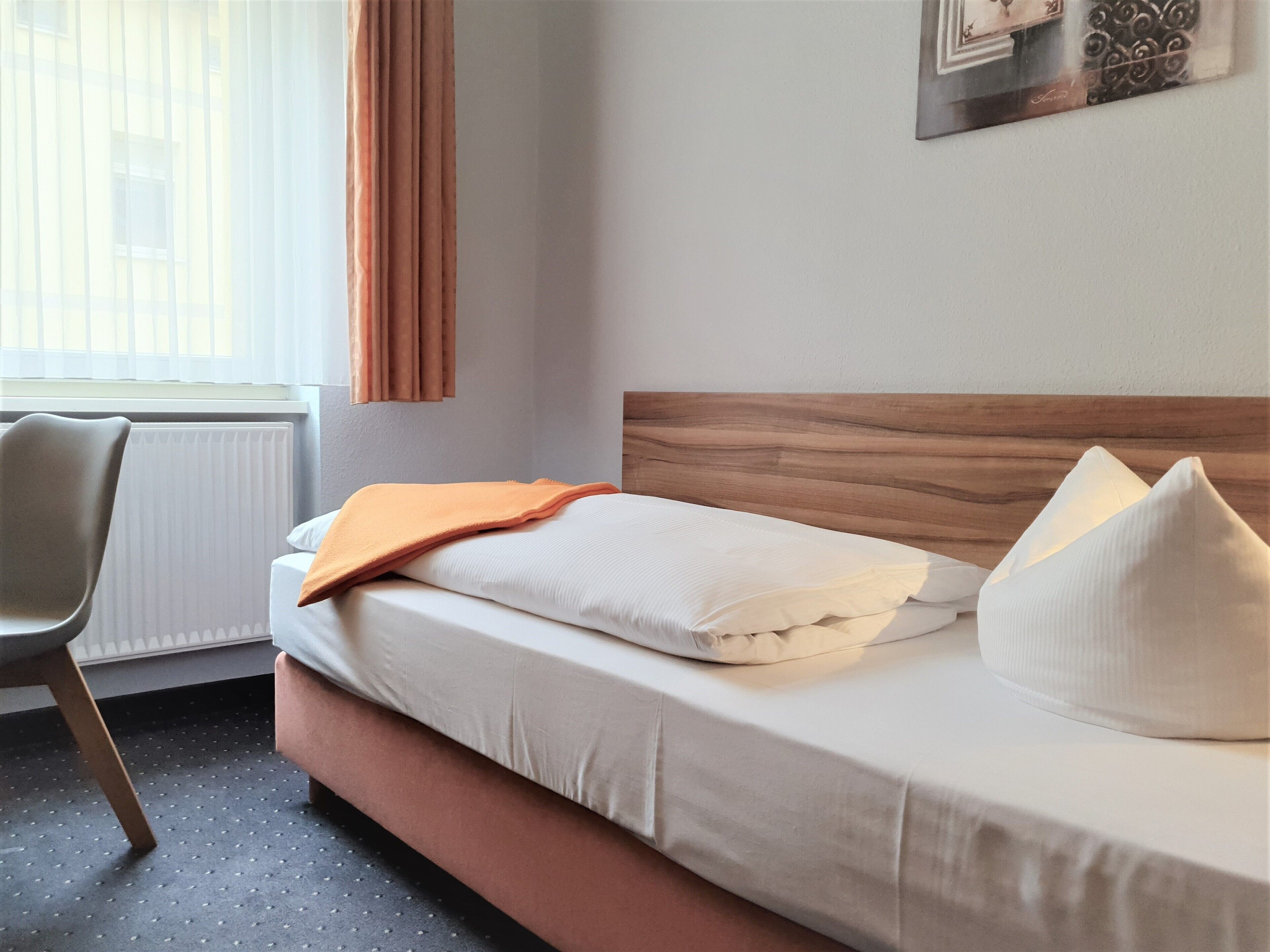 A neatly made bed with a wooden headboard, a chair, and a window with curtains.