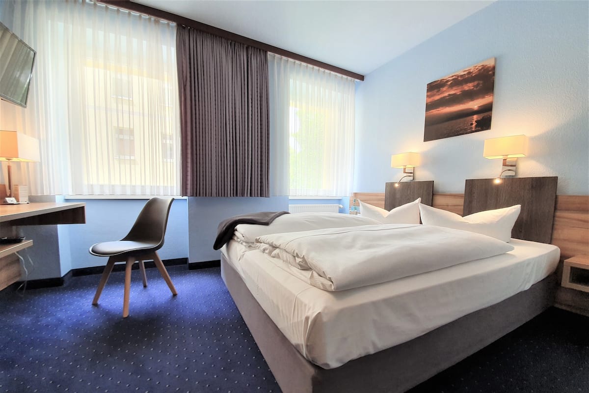 A hotel room with a large bed, a desk, a chair, and two bedside lamps.