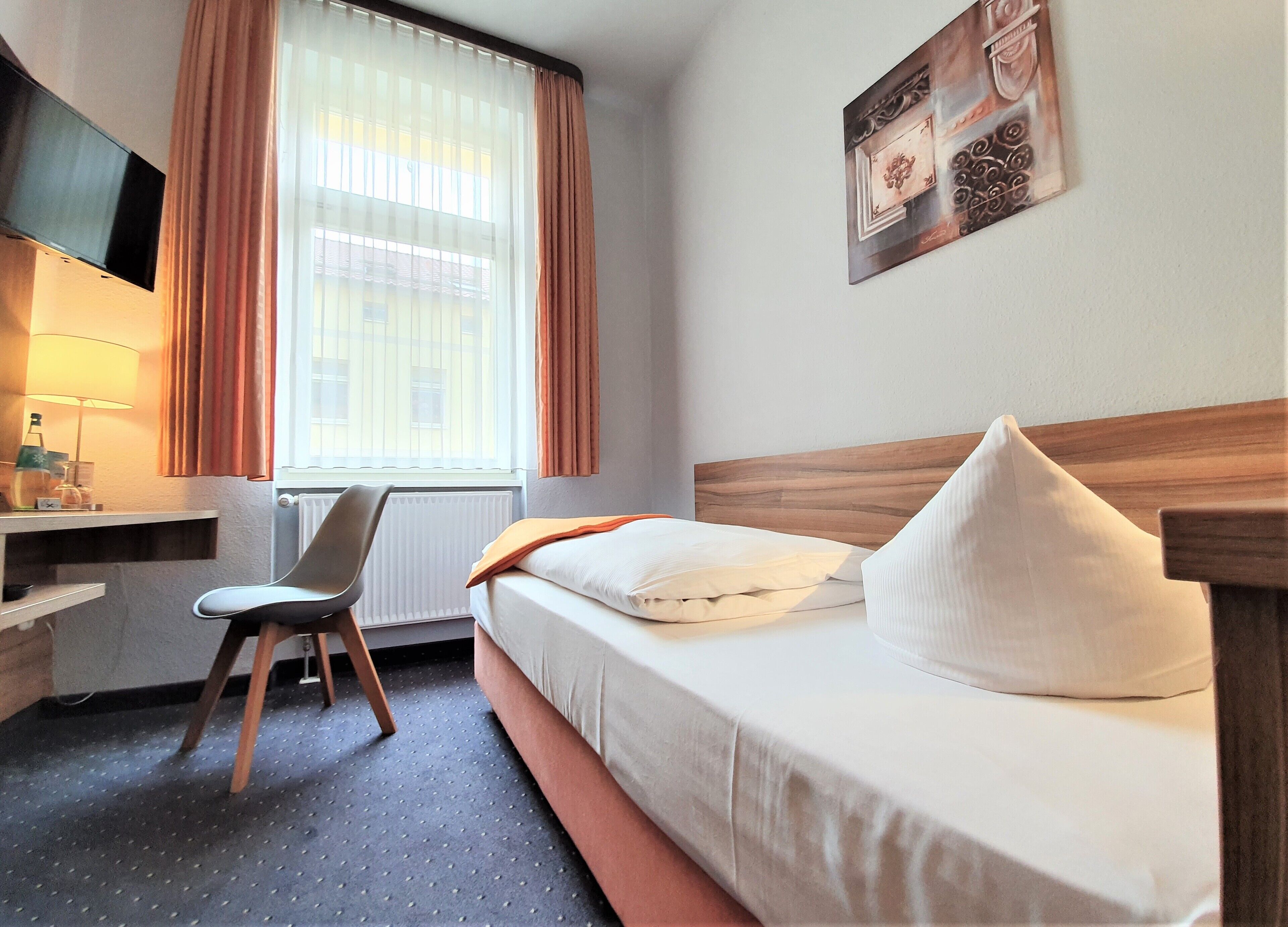 Habitación de hotel con cama, escritorio, silla, televisor y ventana con cortinas.
