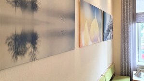 Pared con tres cuadros que muestran escenas naturales, un banco acolchado verde y una ventana con cortinas.