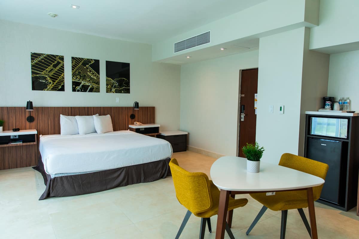 Ein Hotelzimmer mit Bett, Nachttischen, einem Schreibtisch mit Stuhl, einem kleinen Kühlschrank und Bildern an der Wand.