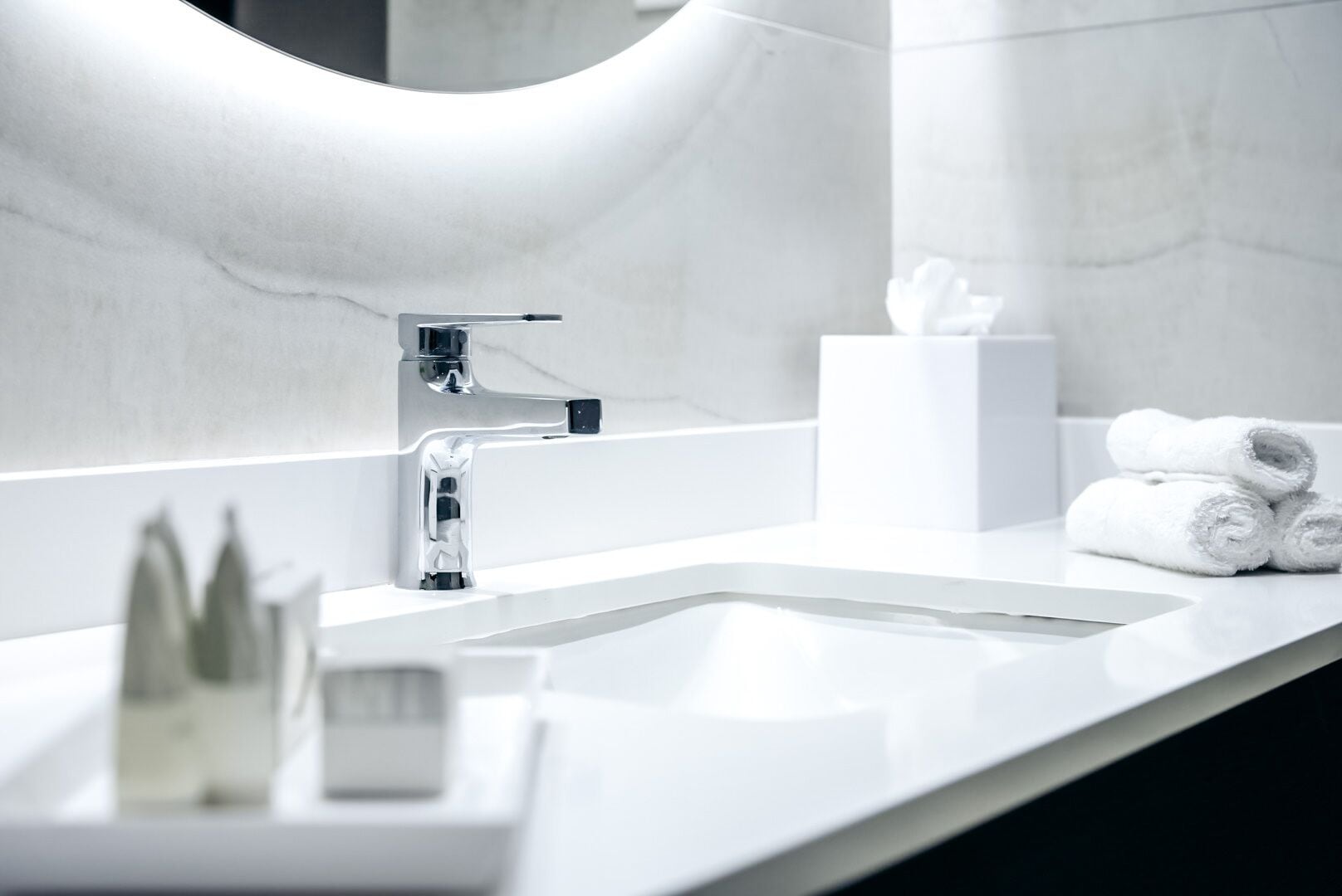 A modern bathroom with a white sink, chrome faucet, and a mirror with a curved frame.