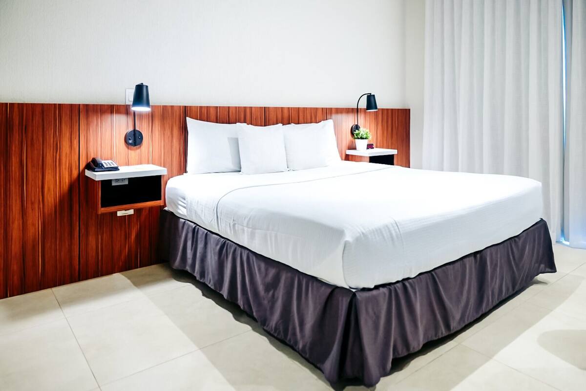 Ein Hotelzimmer mit einem hölzernen Kopfteil, einem großen Bett mit weißen Bettwäsche, zwei Nachttischen mit Lampen und einer kleinen Pflanze auf einem Tisch.