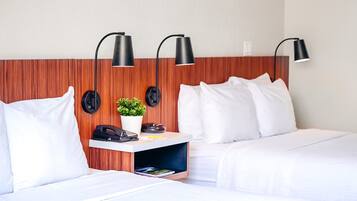 A hotel room with two beds, a desk with a phone and a plant, and three wall-mounted lamps.