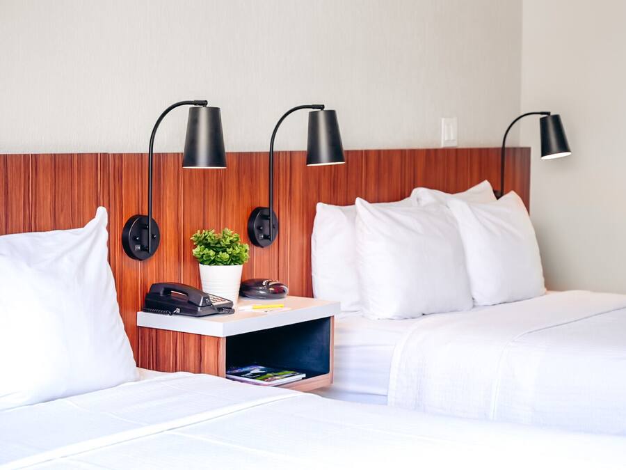 A hotel room with two beds, a desk with a phone and a plant, and three wall-mounted lamps.