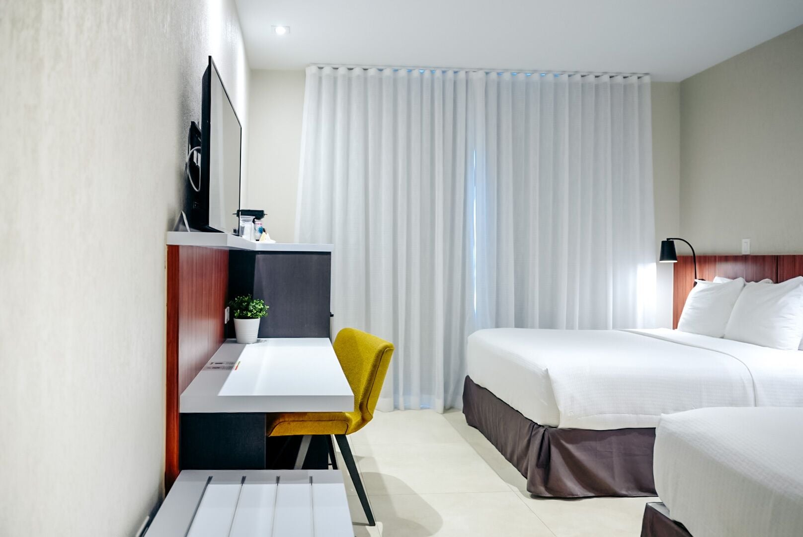 Ein modernes Hotelzimmer mit einem Bett, einem Schreibtisch, einem Sessel, einem Fernseher und einem Fenster mit Vorhängen.