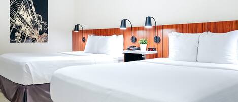 A hotel room with two beds, a wooden headboard, a nightstand, a clock, and a wall-mounted lamp.