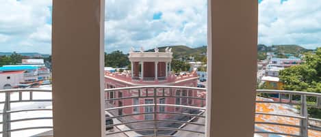 A balcony with a view of a pink building with columns and a dome, surrounded by other buildings and greenery.