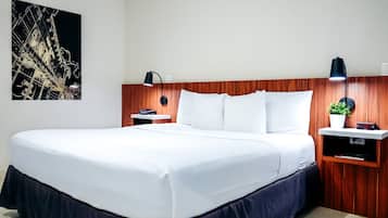 A hotel room with a large bed, wooden headboard, bedside tables with lamps, a small plant, and a wall-mounted clock.