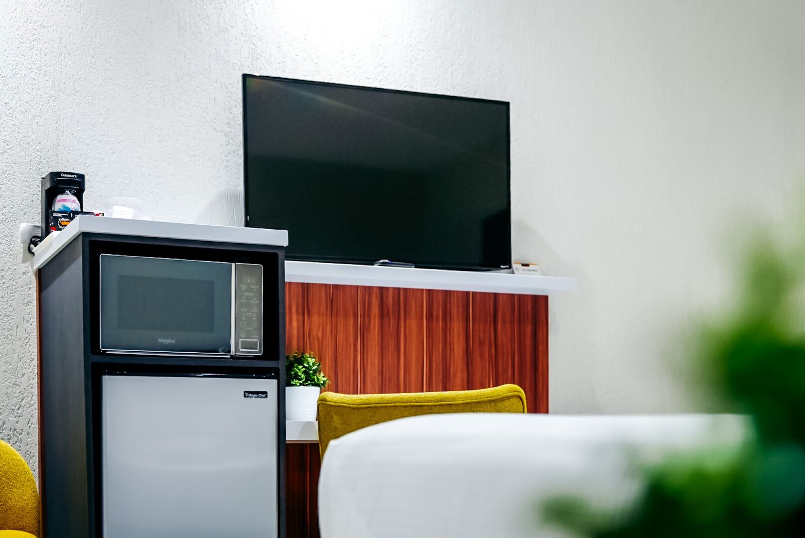 Una kitchenette compacta con microondas, un refrigerador pequeño y un televisor de pantalla plana montado en un mueble de madera.
