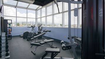 Un gimnasio con equipo de ejercicio, ventanas amplias y vistas a la ciudad.