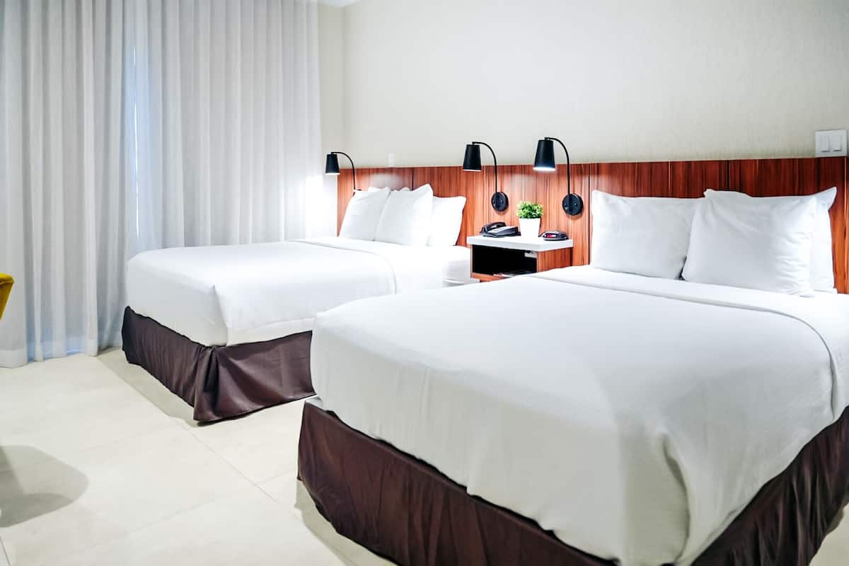 Ein Hotelzimmer mit zwei Betten, einem hölzernen Kopfteil, Nachttischlampen, einem kleinen Tisch mit Pflanze und einem Telefon.