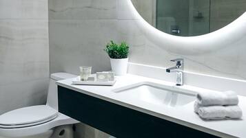 Un baño moderno con inodoro blanco, lavamanos con espejo y zona de ducha.