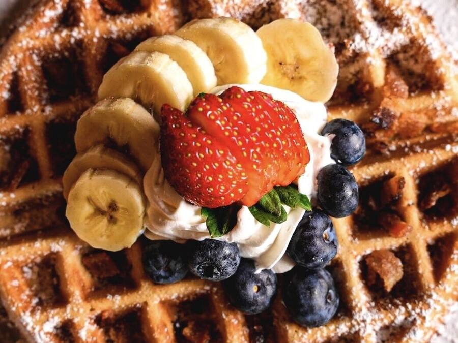 Un waffle coronado con rodajas de plátano, fresas, arándanos y crema batida.
