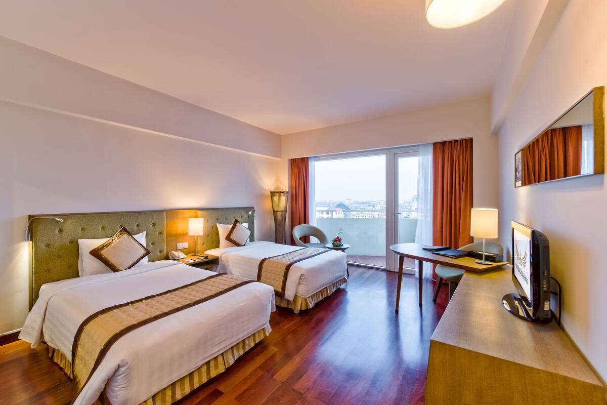Une chambre d’hôtel avec deux lits, un bureau, une chaise, une télévision et une grande fenêtre avec des rideaux.