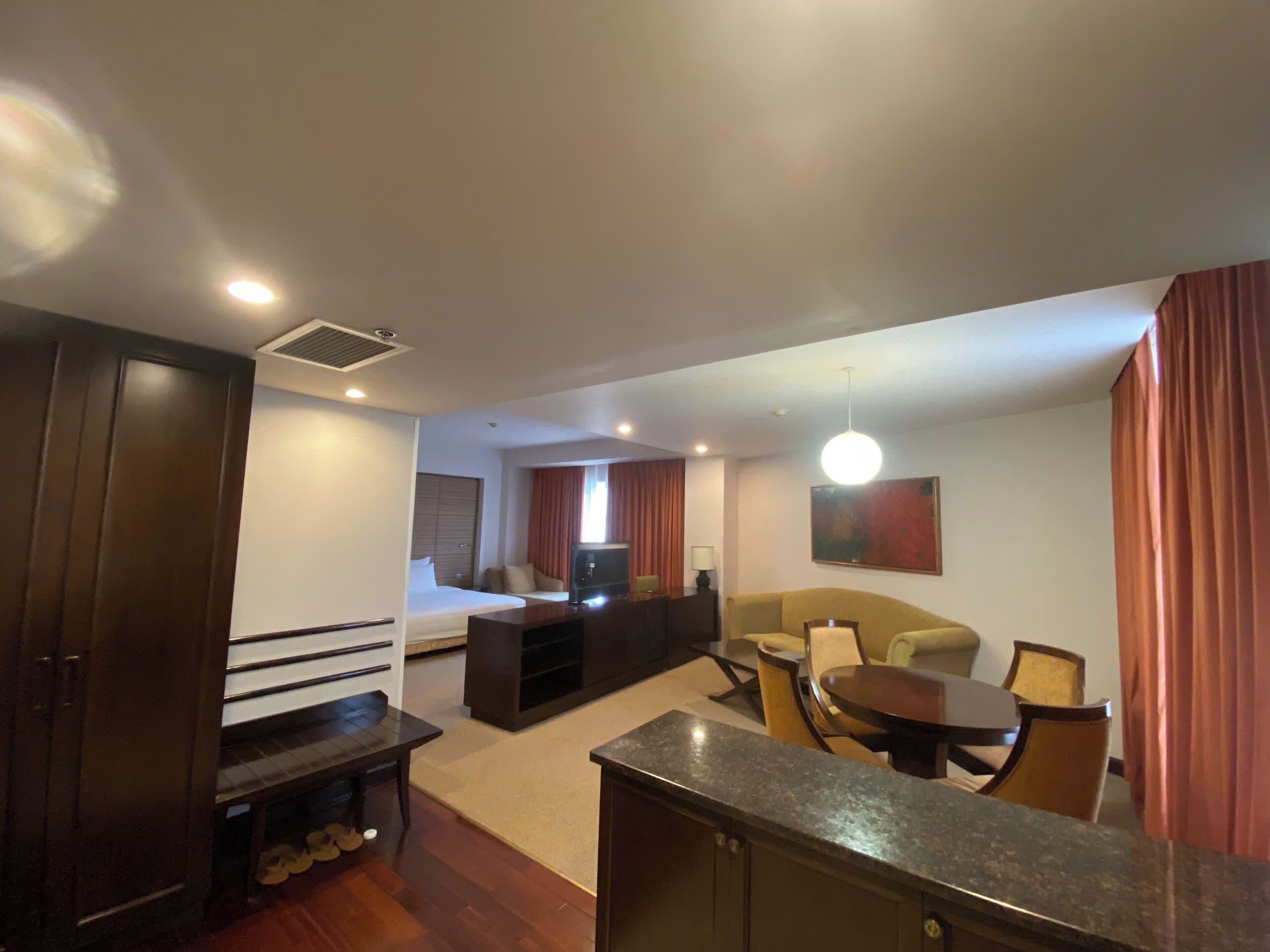 A hotel room with a bed, a TV, a sofa, a dining table, and a kitchen area.