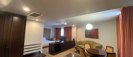 A hotel room with a bed, a TV, a sofa, a dining table, and a kitchen area.