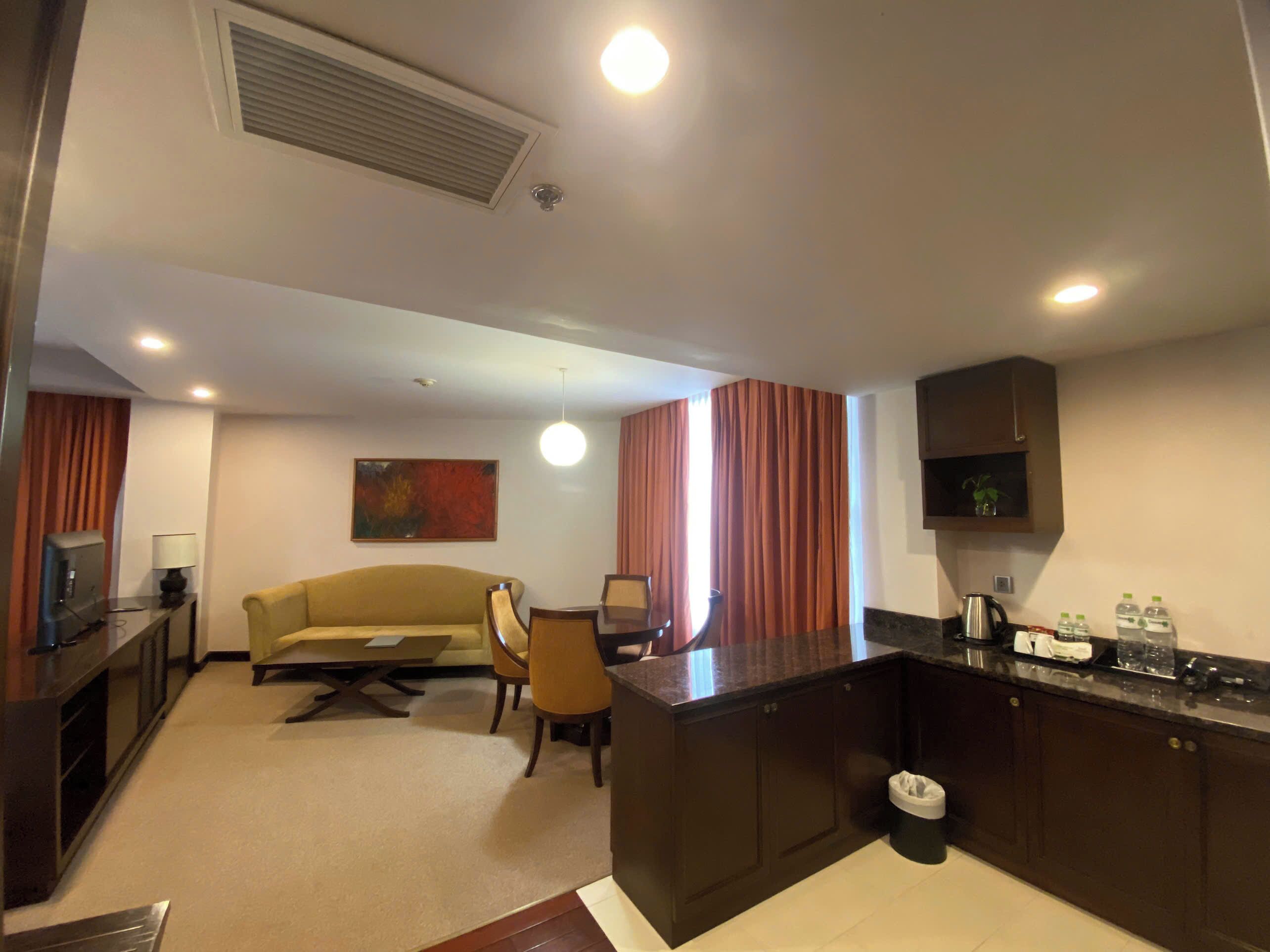 A modern living room with a sofa, dining table, and chairs. There is a kitchen area with cabinets and a countertop.