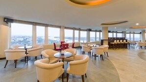 Un espace intérieur vaste et bien aménagé, avec de nombreux coins salon, de grandes fenêtres offrant une vue sur la ville et un design de plafond moderne.