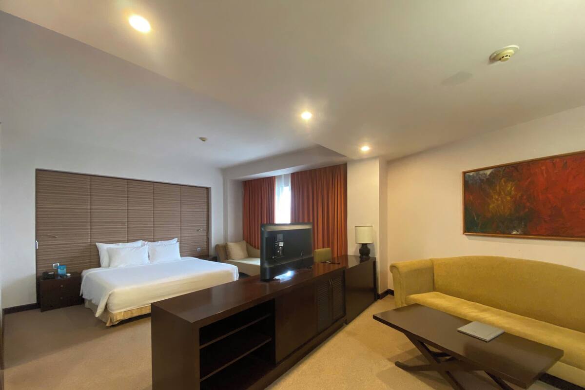 Une chambre d’hôtel avec un lit, une télévision, un canapé, un bureau et un tableau au mur.