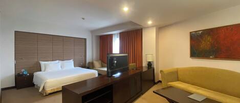 A hotel room with a bed, a TV, a sofa, a desk, and a painting on the wall.