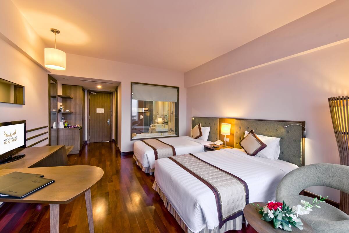 Une chambre d’hôtel avec deux lits, un bureau, une chaise et une télévision.