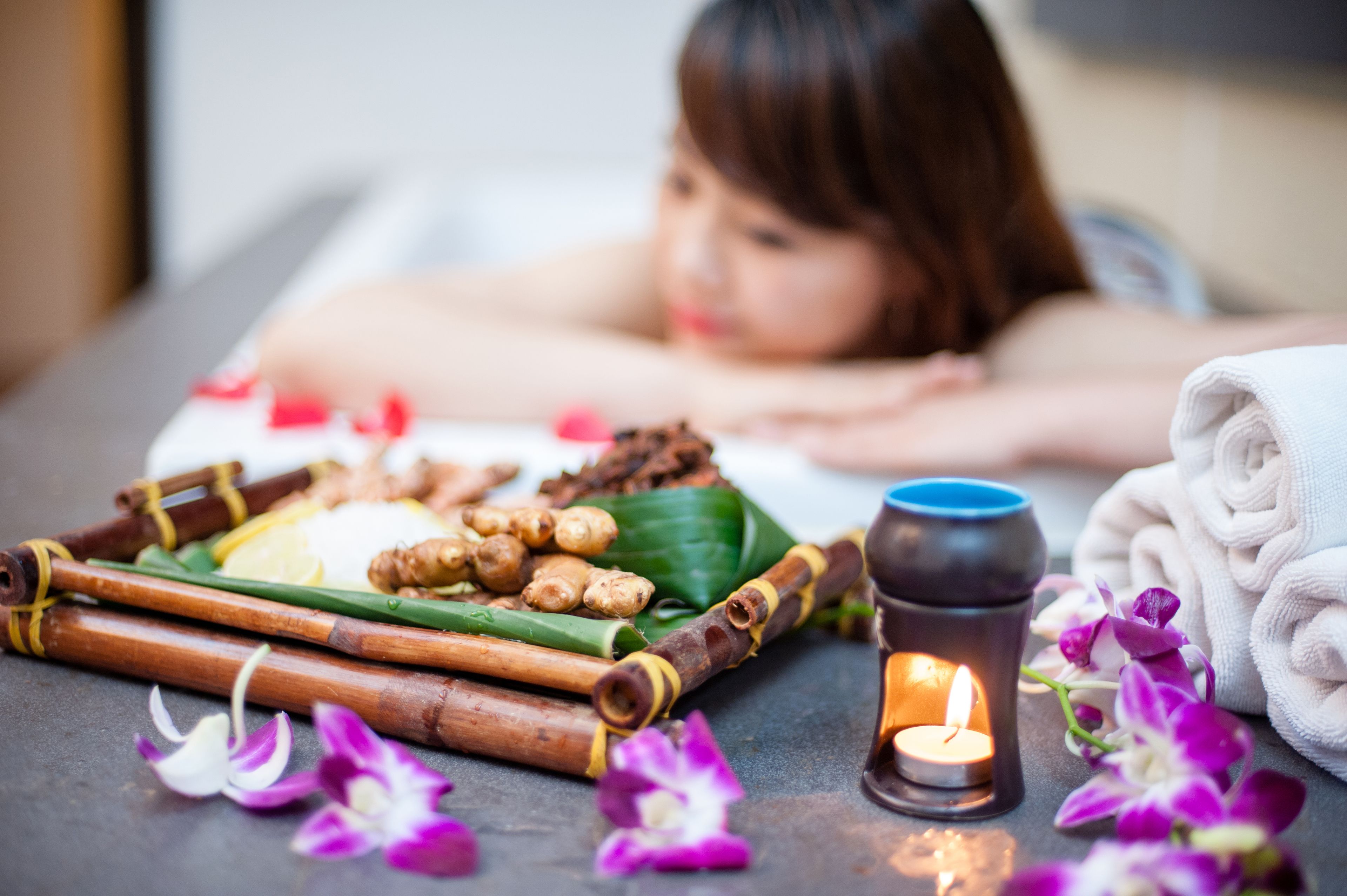 A spa setting with a massage table, a tray of ginger and lemongrass, a candle, and a towel.