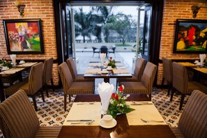 A restaurant with a brick wall, framed artwork, and a table set for two with chairs. - Muong Thanh Holiday Hue Hotel (Hue)