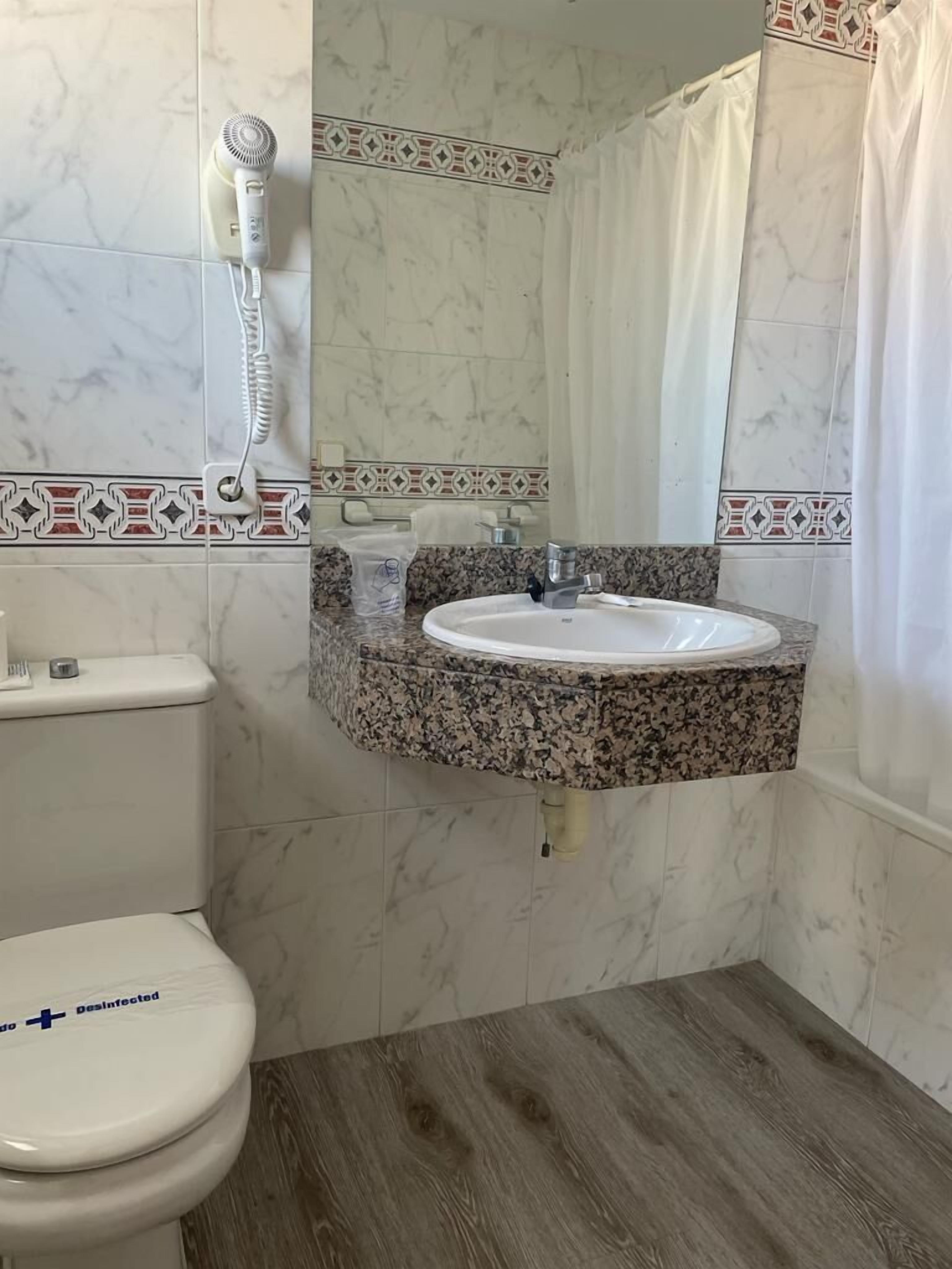 Un bagno con un WC, un lavandino, un asciugacapelli e una tenda per la doccia.