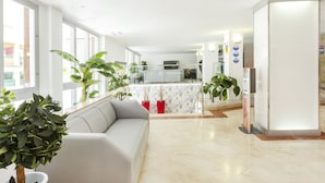 A modern living room with a sofa, potted plants, and a kitchen area in the background. - Hotel Kilimanjaro (Llucmajor)