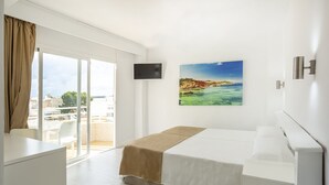 A hotel room with a bed, a desk, a TV, and a large window with a view of the city. - Hotel Kilimanjaro (Llucmajor)