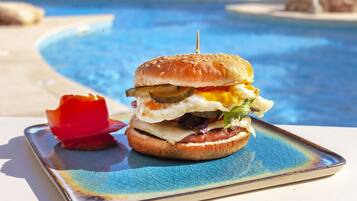 Hamburguesa con un palillo sobre un plato, colocada junto a una piscina.