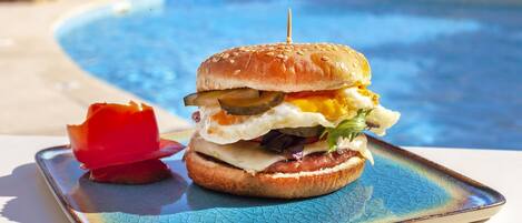 Un hamburger, maintenu par un cure-dent, est posé sur une assiette, près d’une piscine.