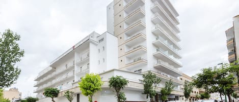 Un hotel de varios pisos con balcones, un letrero que indica que es un hotel y varios automóviles estacionados en la calle.