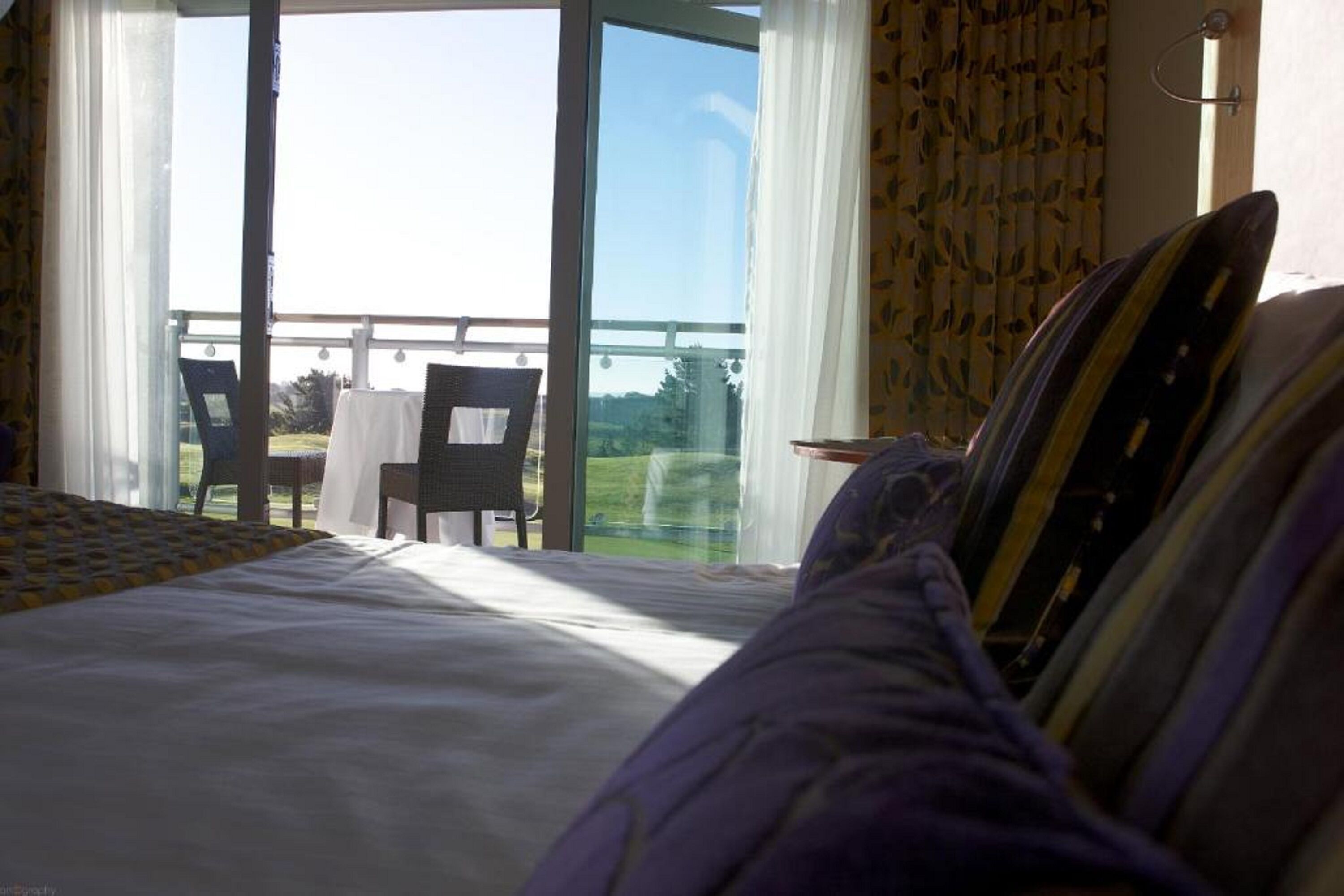 Un dormitorio con una cama grande, vistas al exterior a través de un ventanal corredero y una silla junto a la puerta.
