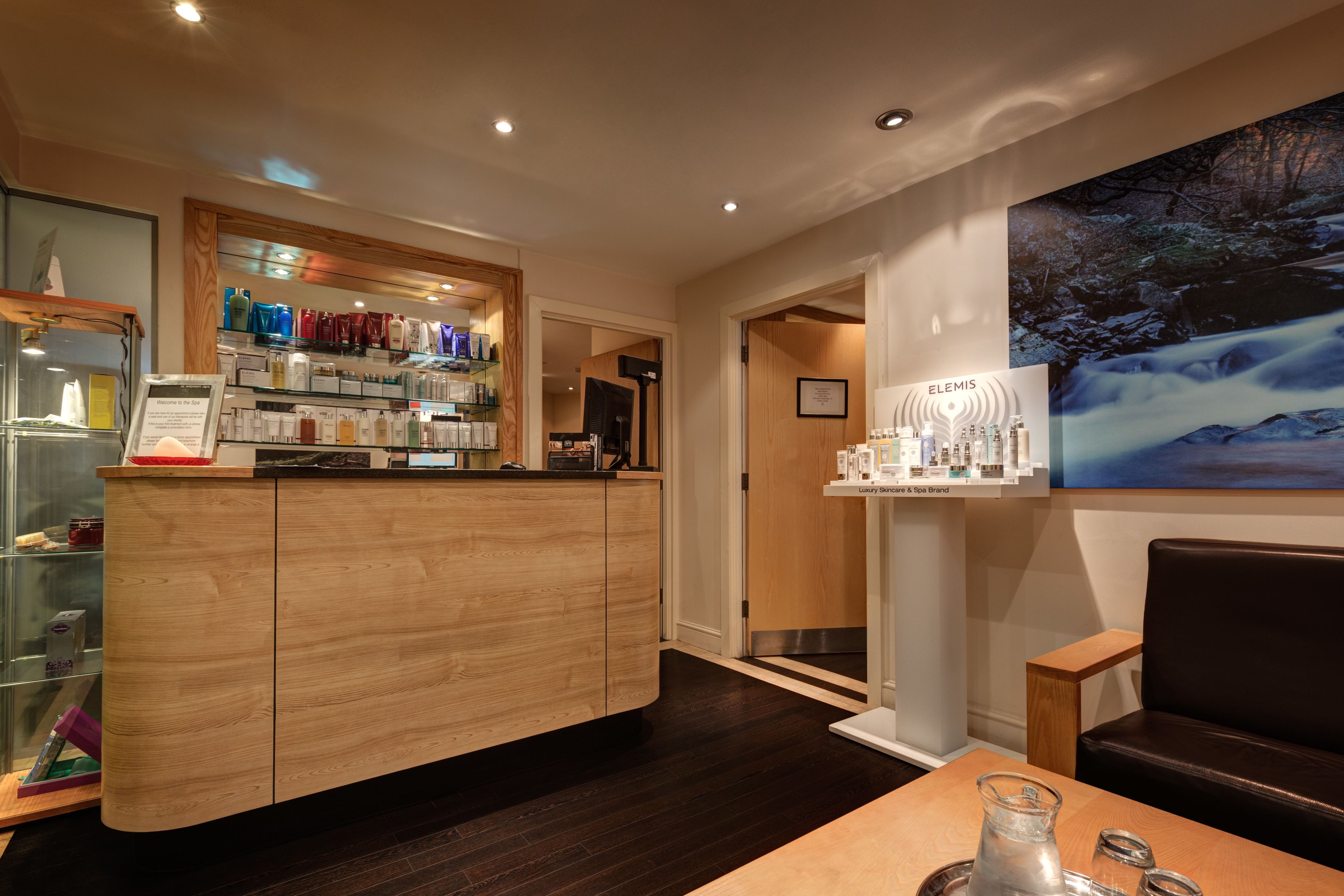 A modern hotel lobby with a wooden reception desk, a glass display case, and a large painting of a waterfall.