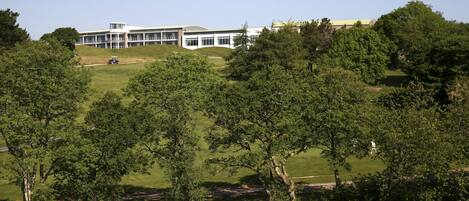 A large building with multiple floors and a flat roof, surrounded by lush greenery and trees.