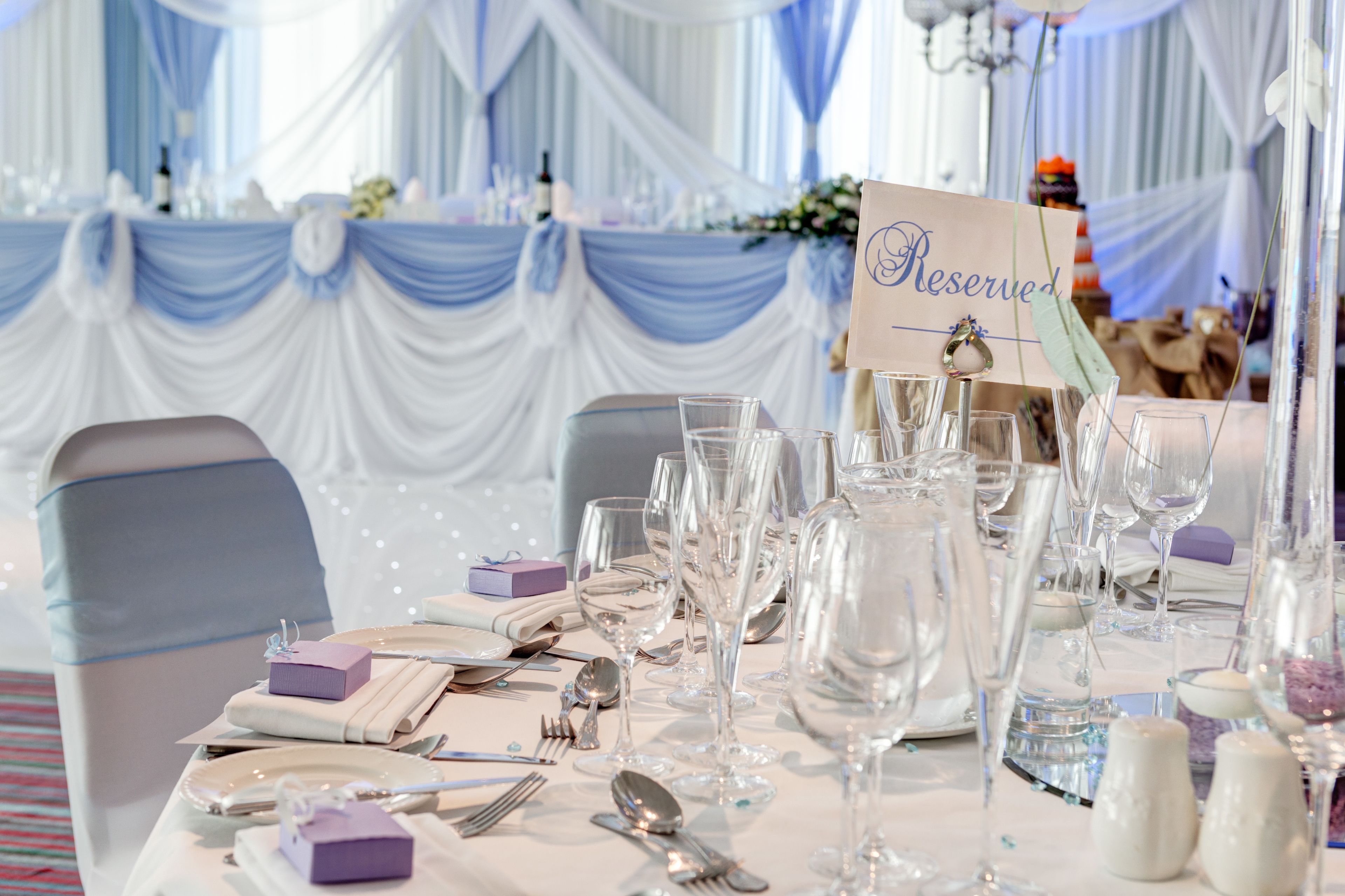 A table set for a formal event with a 'Reserved' sign, white drapery, and a chandelier.