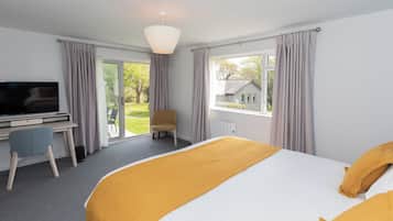 A hotel room with a bed, a desk with a chair, a television, and a view of a house through the window.