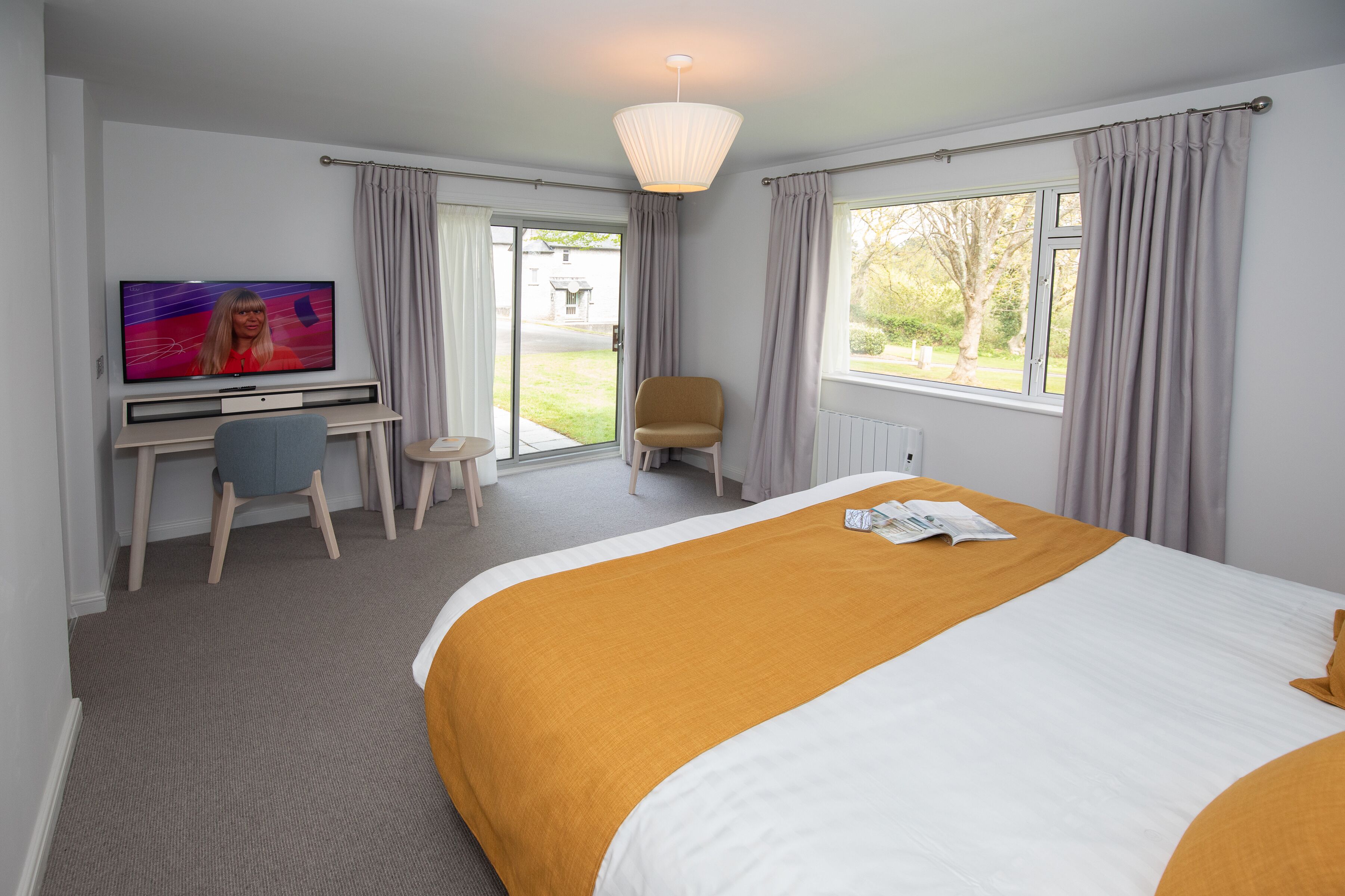 Ett hotellrum med en stor säng, en tv, ett skrivbord med en stol och utsikt över omgivningarna.