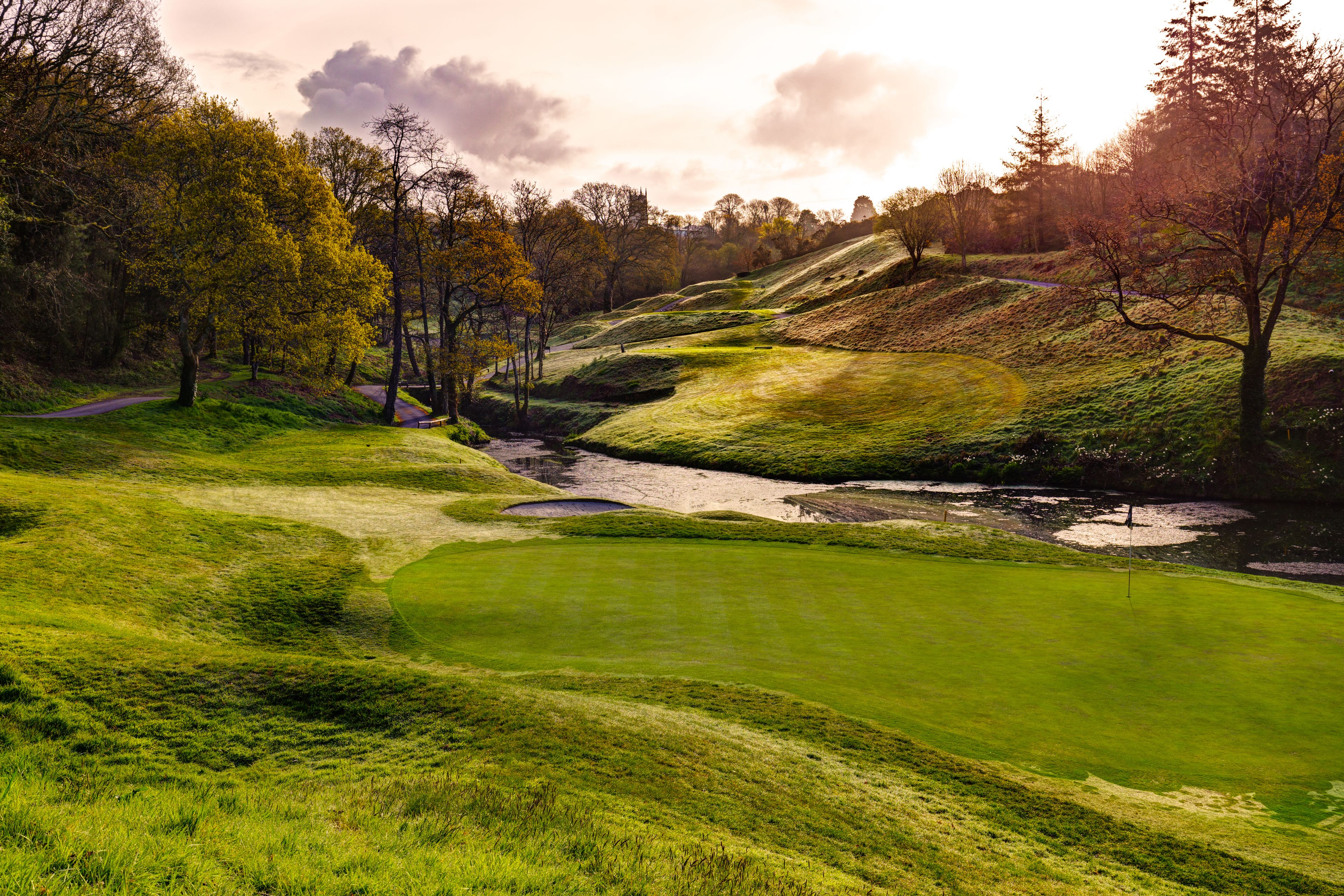 Golfkenttä, jossa on vesiesteitä, puita ja kirkas taivas.