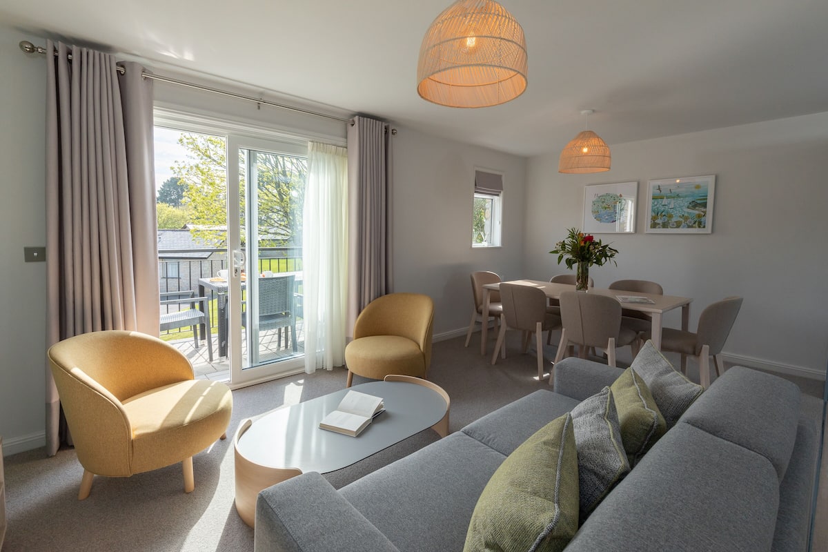 Una sala moderna con un sofá gris, dos sillones, una mesa de centro y un comedor con una mesa y sillas.