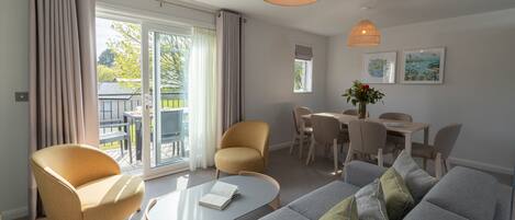 Una sala moderna con un sofá gris, dos sillones, una mesa de centro y un comedor con una mesa y sillas.