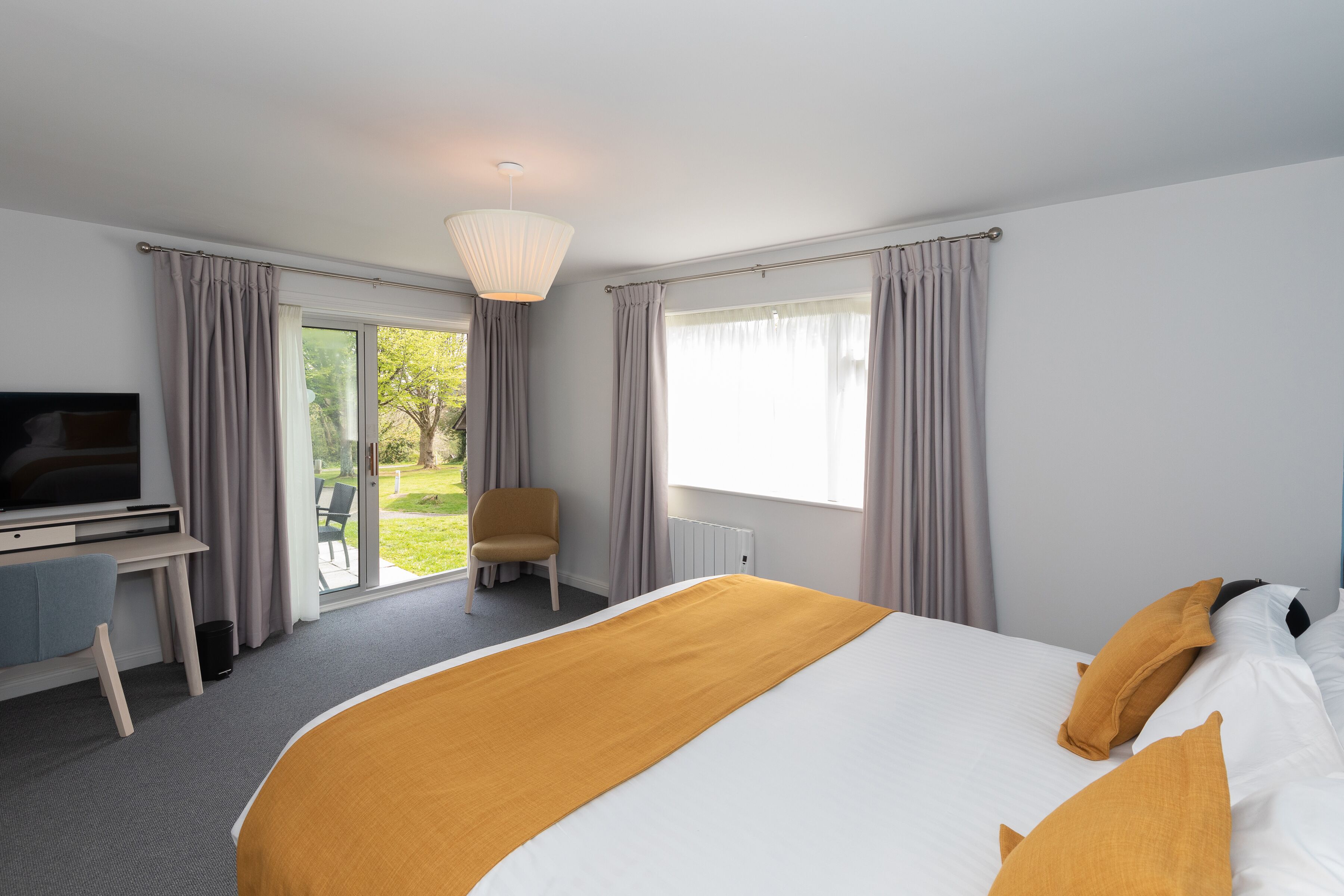 A hotel room with a bed, a desk, a television, and a view of the outdoors.