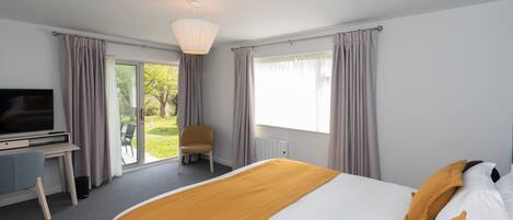 A hotel room with a bed, a desk, a television, and a view of the outdoors.