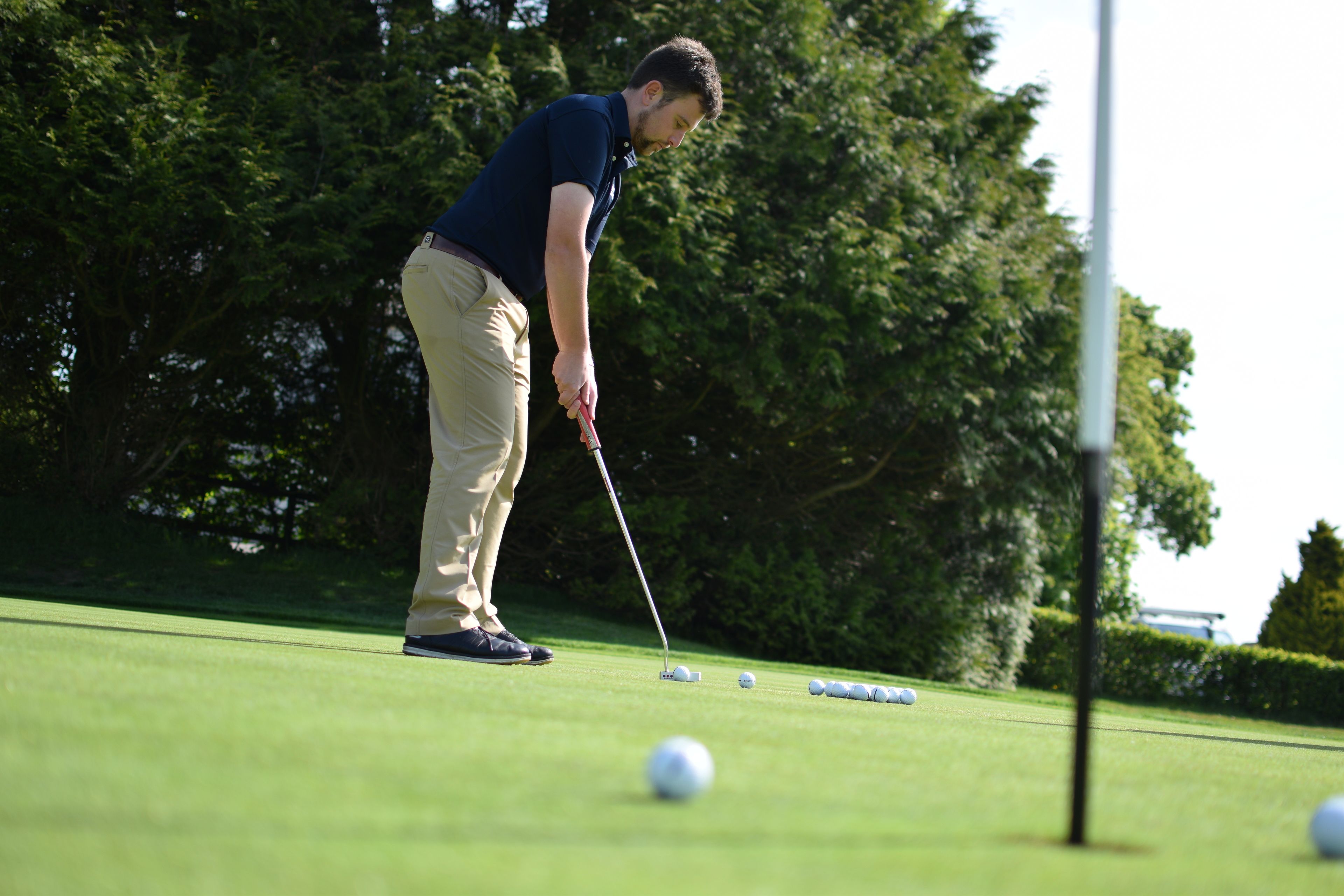 Una persona gioca a golf su un campo curato, con alberi sullo sfondo.