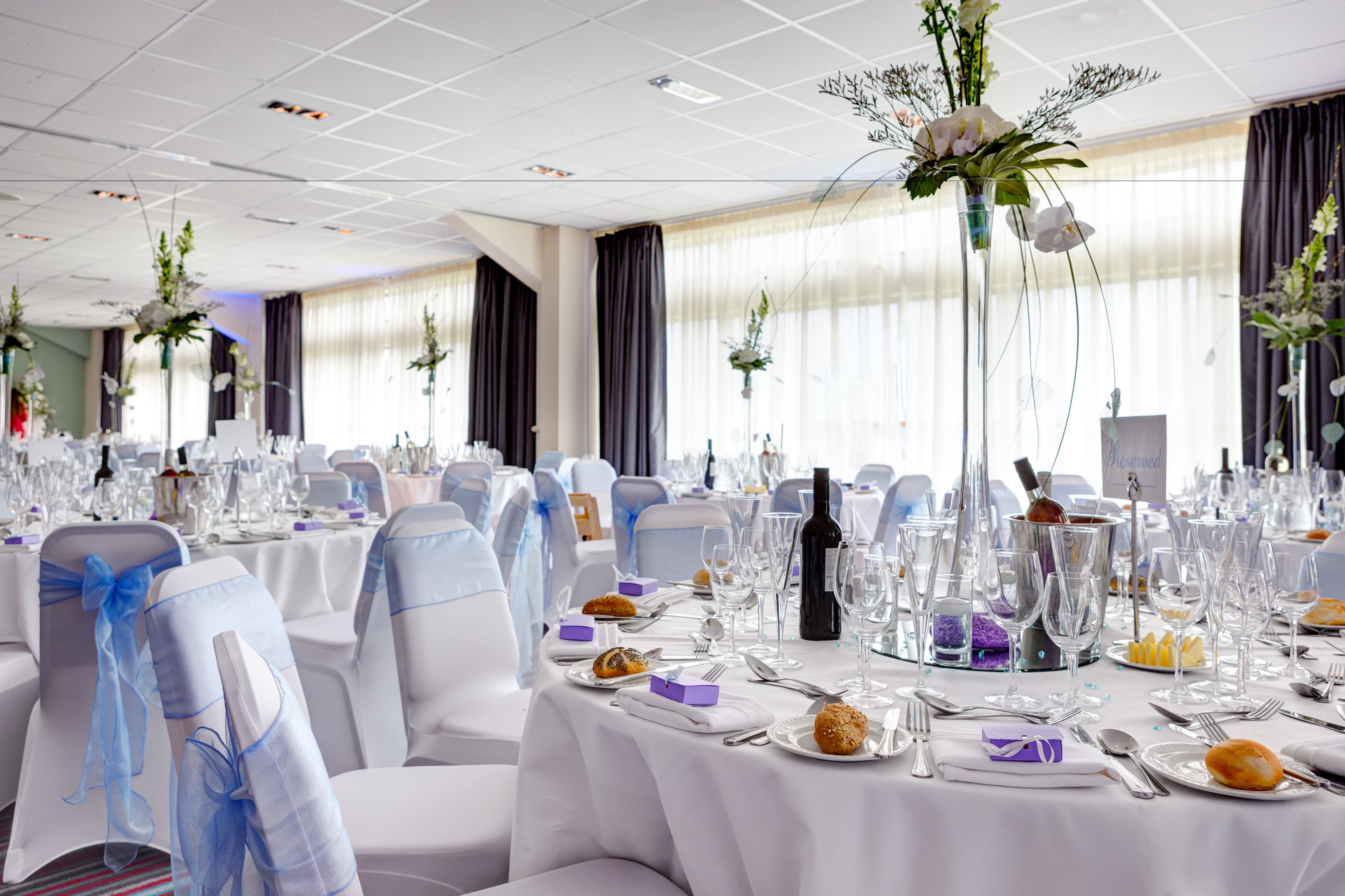 A banquet hall with round tables set for a formal event, complete with chairs, table settings, and floral centerpieces.