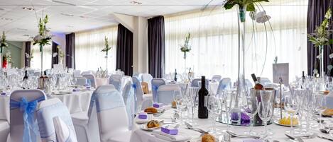 A banquet hall with round tables set for a formal event, complete with chairs, table settings, and floral centerpieces.