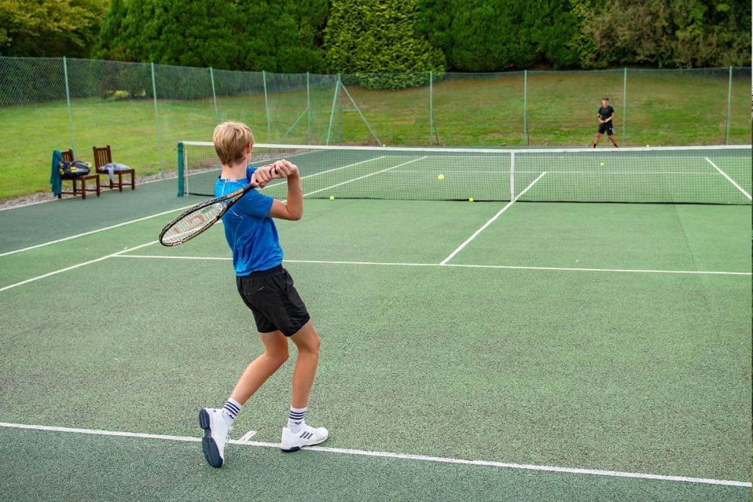 A tennis court with a net, chairs, and a fence.