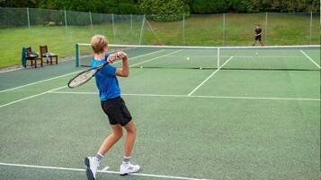 Cancha de tenis con red, sillas y valla.